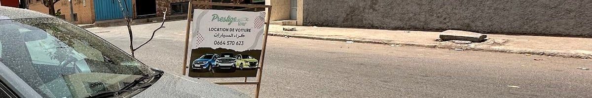 Une Dacia Sandero grise garée rue 56 à côté du panneau « Prestige tour · Location de voiture · كراء السيارات · 0664 570 623 »